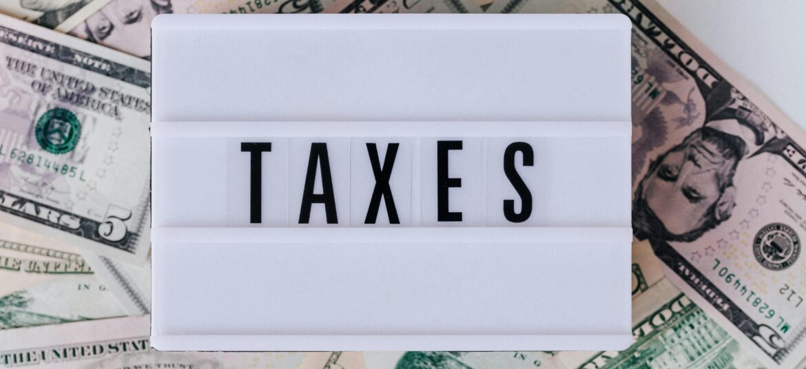 Top view of white vintage light box with TAXES inscription placed on stack of USA dollar bills on white surface