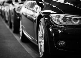 Close-up black and white image of a luxury car line-up focusing on vehicle headlights.
